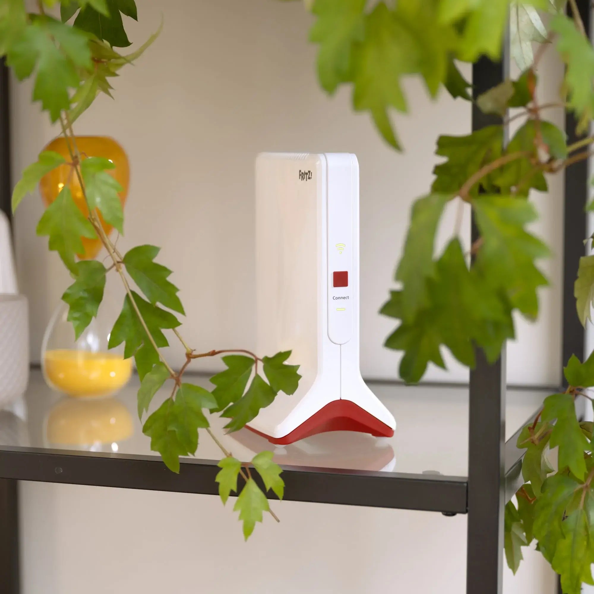 Modernes Gerät auf einem Regal, umgeben von Pflanzen, in einer hellen, minimalistischen Umgebung.