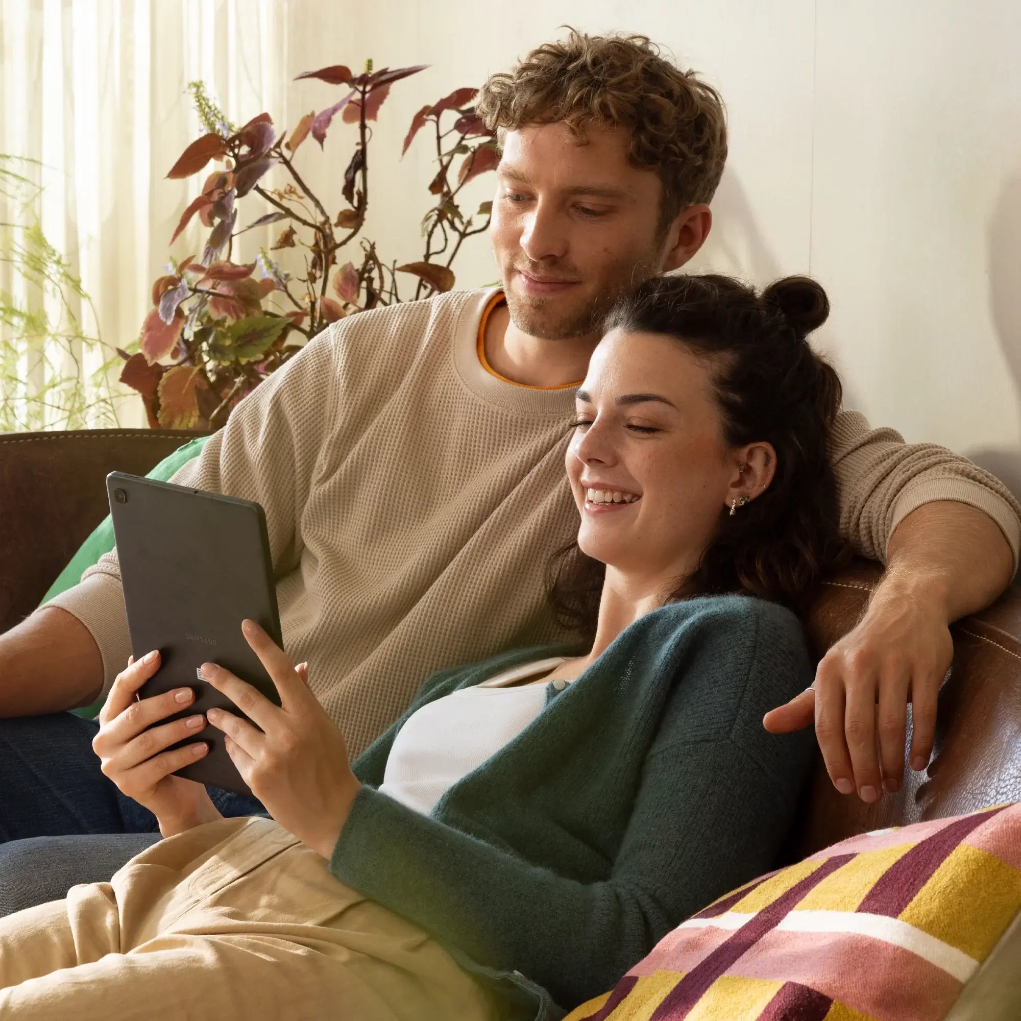 Paar entspannt auf der Couch und schaut gemeinsam auf ein Tablet, umgeben von natürlichem Licht.